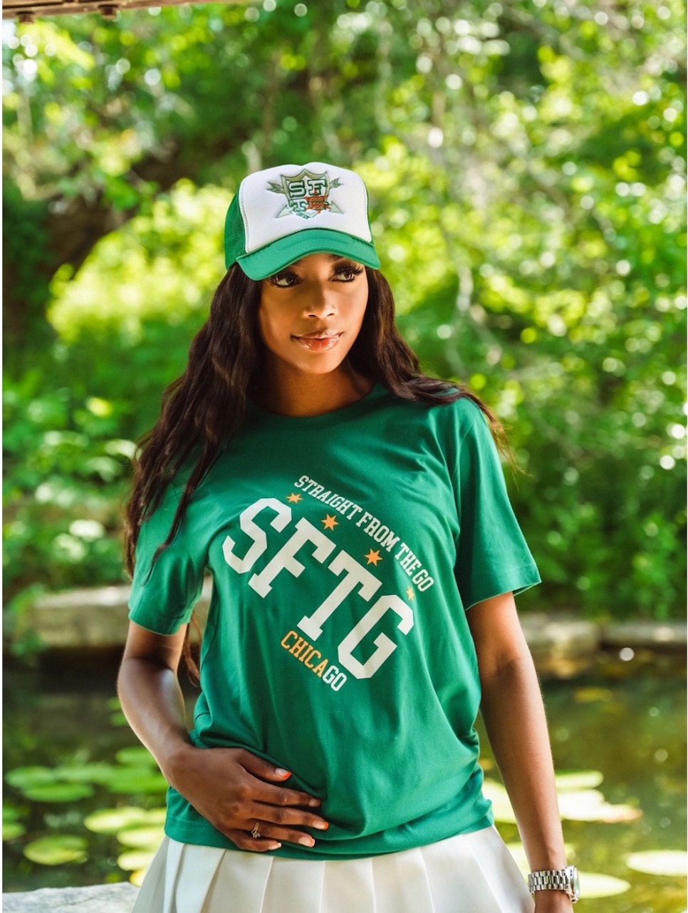 Raven smith standing wearing a white and green trucker hat with the SFTG shield Logo, with a hunter green SFTG t-shirt